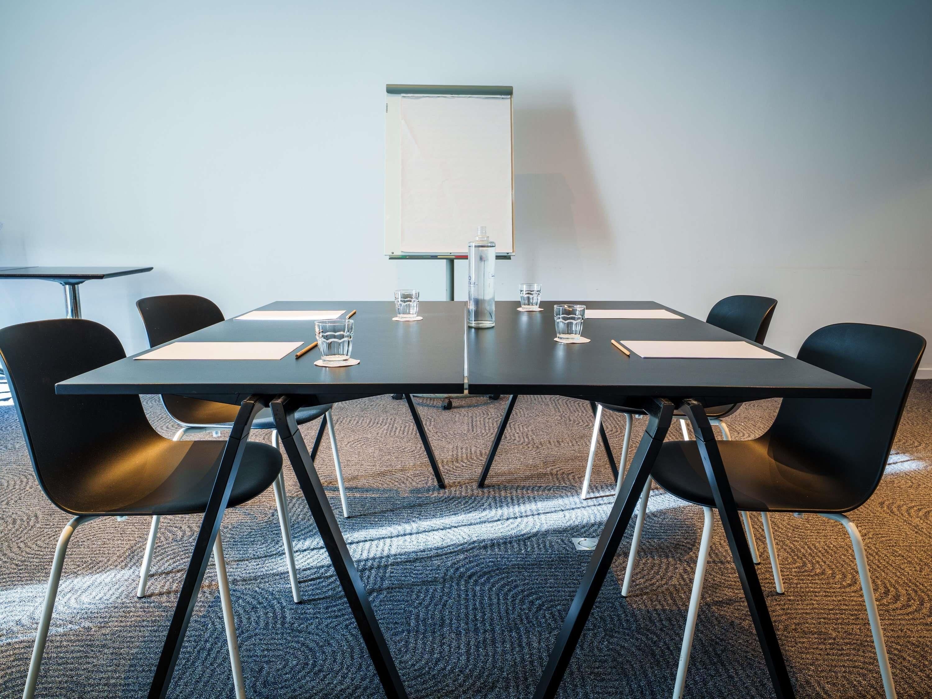 A conference room with a black table, six black chairs, a whiteboard, and a carpeted floor.