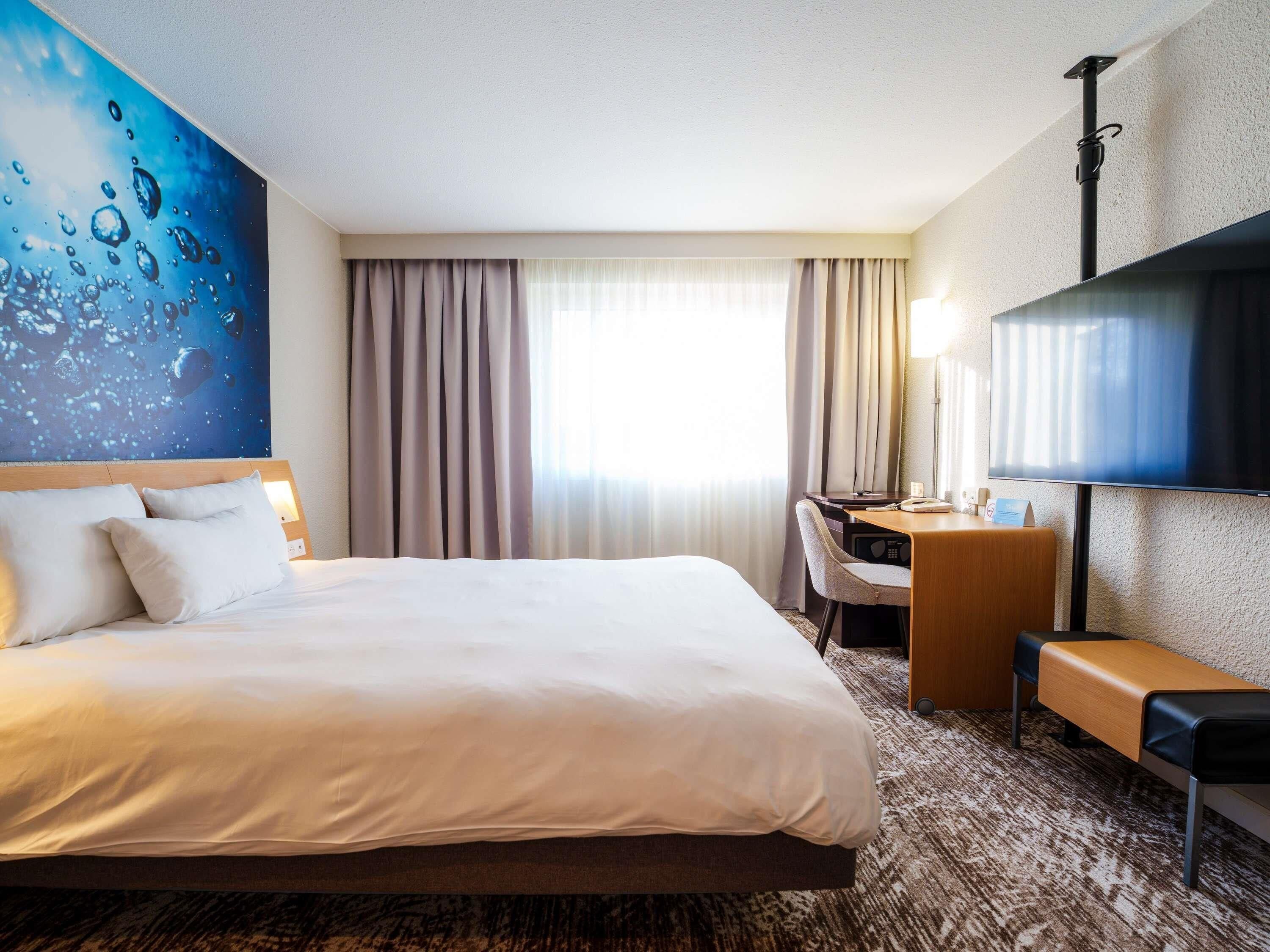 Una habitación de hotel con una cama grande, un escritorio con una silla, un televisor de pantalla plana y un cuadro en la pared.