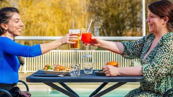 Dos personas brindando con bebidas en una mesa al aire libre, con una piscina al fondo.