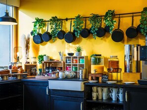 Una cocina con ollas colgantes, frascos de condimentos, una cafetera y un letrero que indica una barra de café y zumo de naranja.