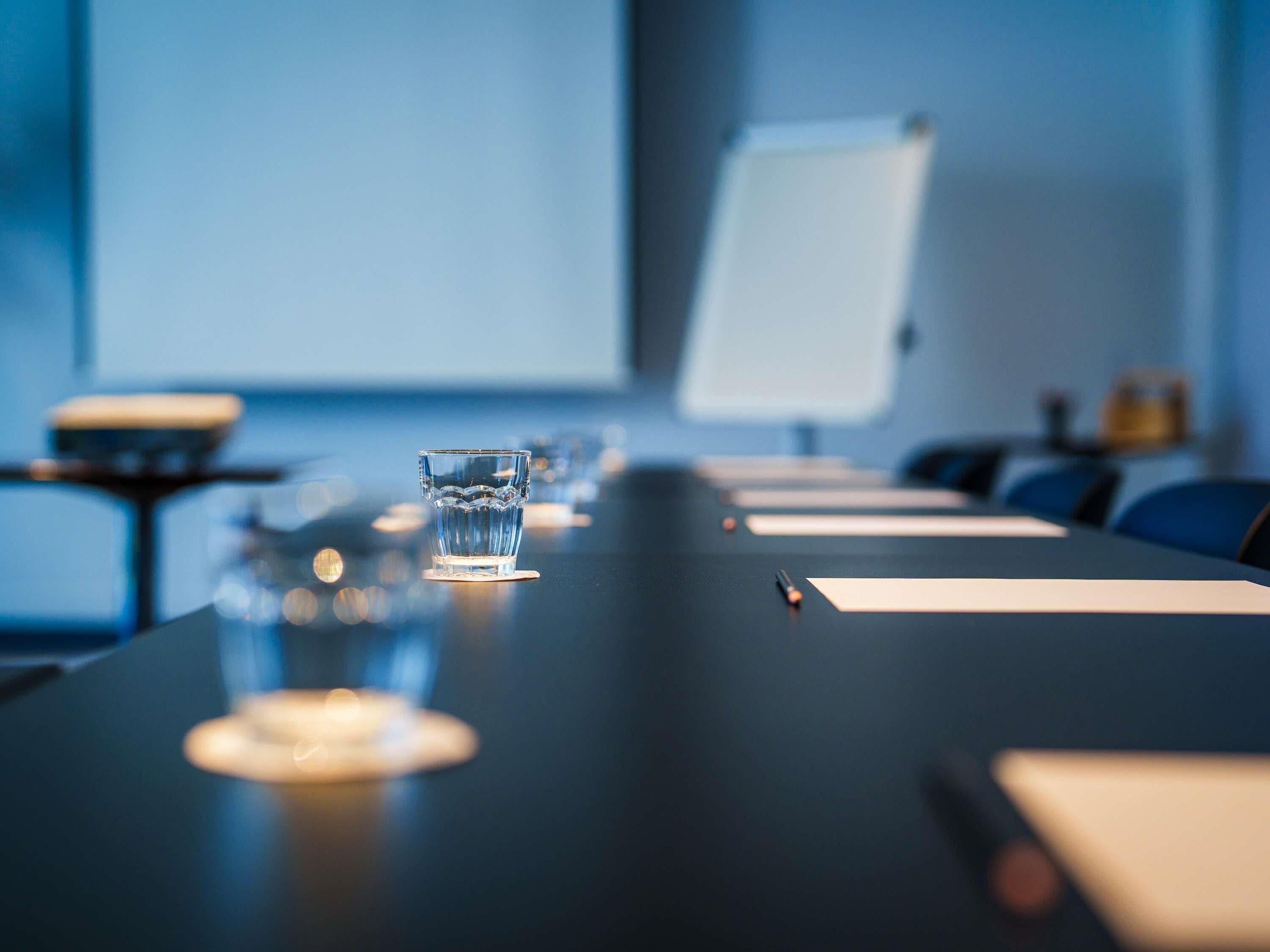 Une salle de conférence avec une longue table, des verres d’eau et un tableau blanc en arrière-plan.