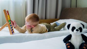 A child lying on a bed with a panda plush toy and a wooden toy structure.
