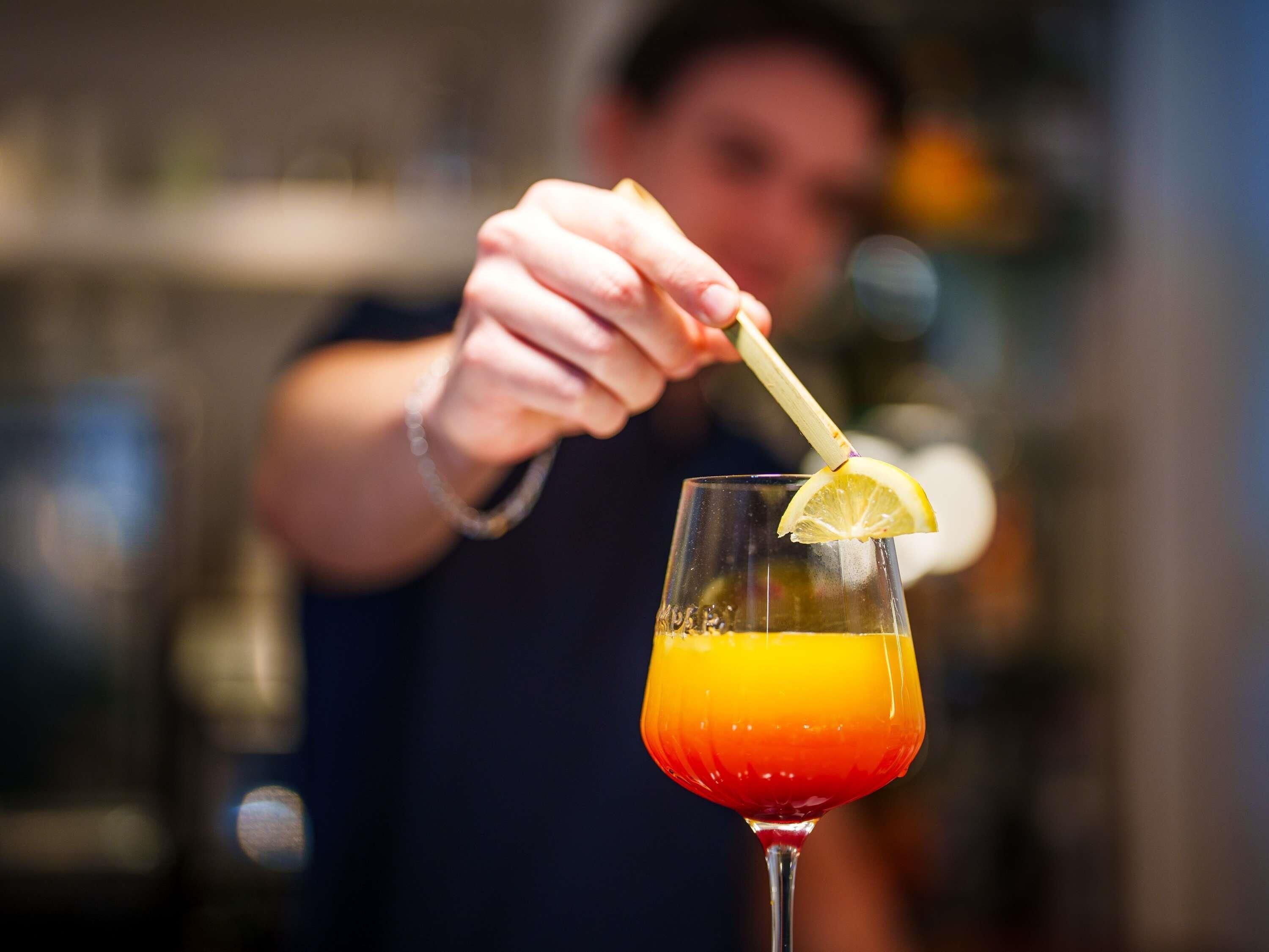 A person garnishing a cocktail with a lemon slice.