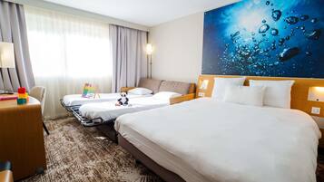 A hotel room with two beds, a desk, a lamp, and a wall painting.