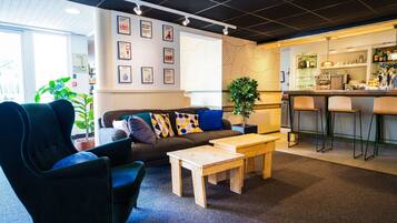 A modern lounge area with a sofa, armchairs, a coffee table, and a bar with stools.
