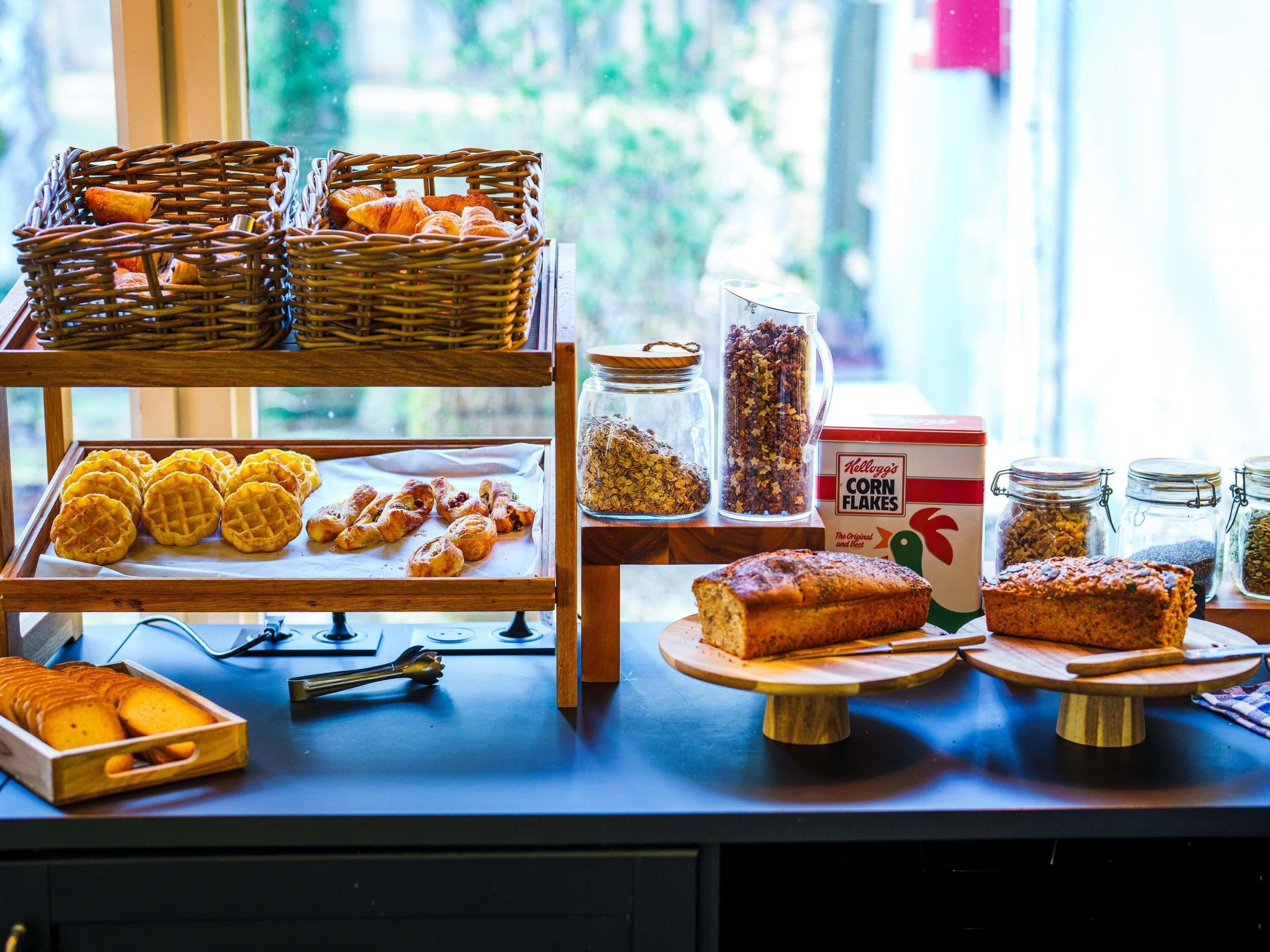 A breakfast buffet with various pastries, a loaf of bread, and jars of cereal.