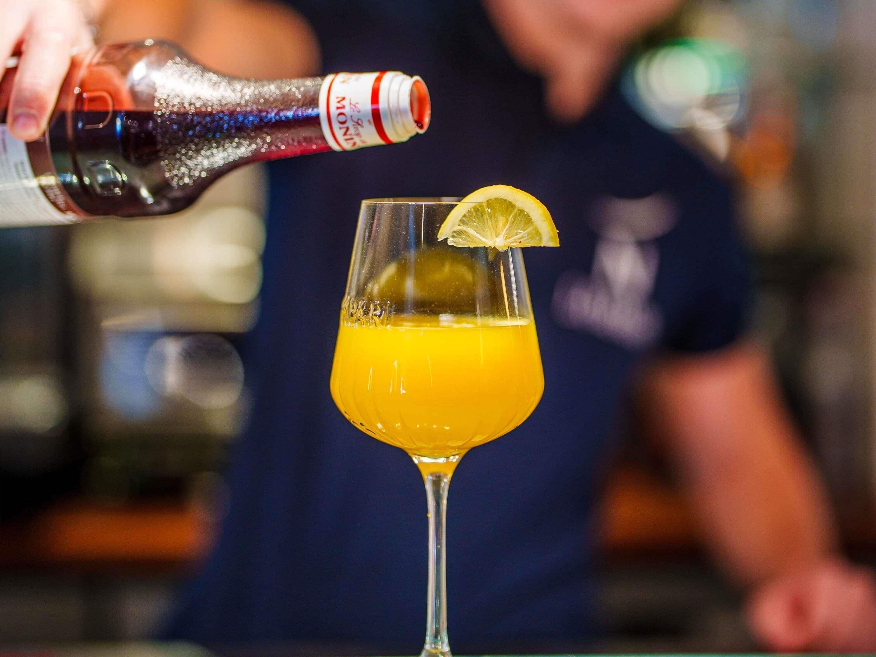 A cocktail being poured into a glass with a lemon garnish.