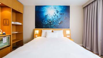 Ein Hotelzimmer mit einem großen Bett, einem Holzschrank, einem Schreibtisch mit Lampe sowie einem Bild von Wassertropfen an der Wand.