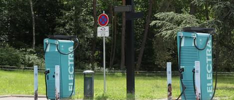 Dos estaciones de carga para vehículos eléctricos con la etiqueta 'ELECTRA', códigos QR y una señal de no estacionamiento al fondo.