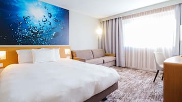 Una habitación de hotel con una cama grande, un sofá, un escritorio y una ventana con cortinas.