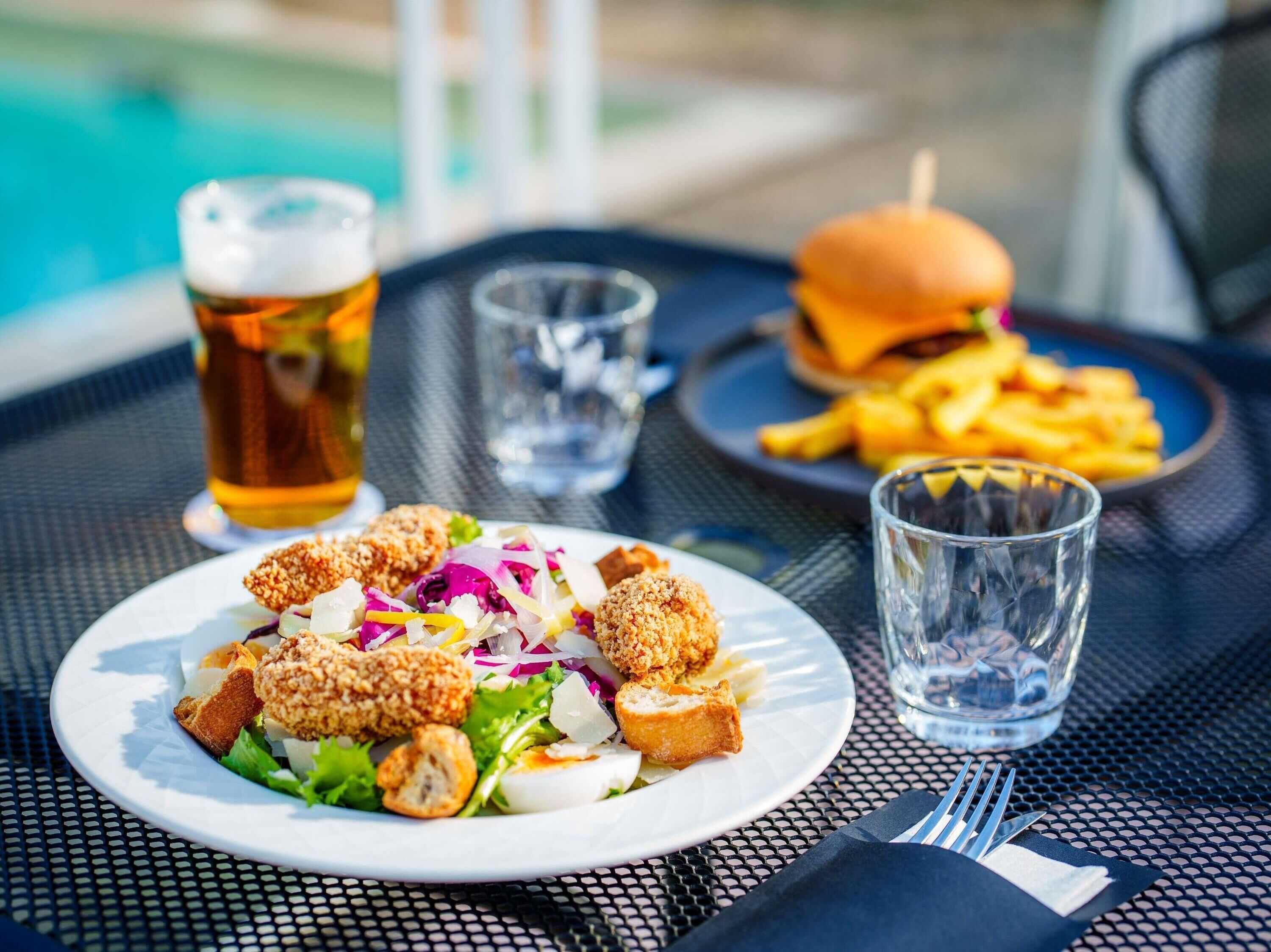 A meal with a salad, burger, and fries on a table with a pool view.