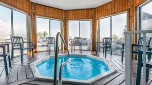 A wooden deck with a hot tub, chairs, and large windows offering views of the surrounding area. - Ramada by Wyndham Mackinaw City Waterfront (Mackinaw City)