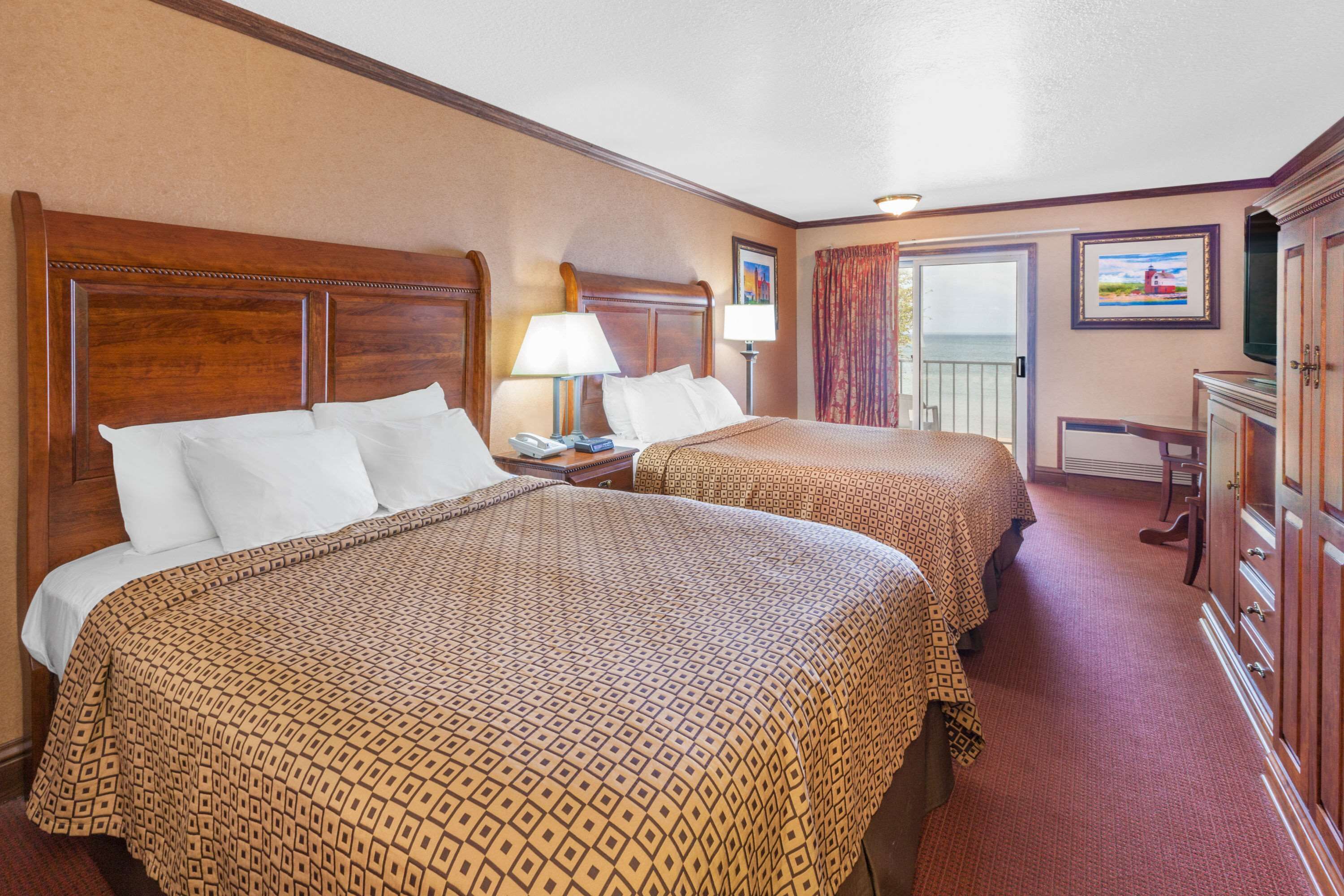 A hotel room with two beds, a desk, a chair, a television, and a door leading to a balcony.