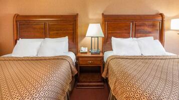 A hotel room with two beds, each with a wooden headboard, a bedside table with a lamp, and a patterned bedspread.