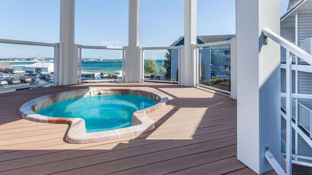 A covered outdoor swimming pool with a view of the sea and a parking area in the background. - Ramada by Wyndham Mackinaw City Waterfront (Mackinaw City)