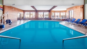 An indoor swimming pool with clear blue water, wooden walls, and blue lounge chairs. - Ramada by Wyndham Mackinaw City Waterfront (Mackinaw City)
