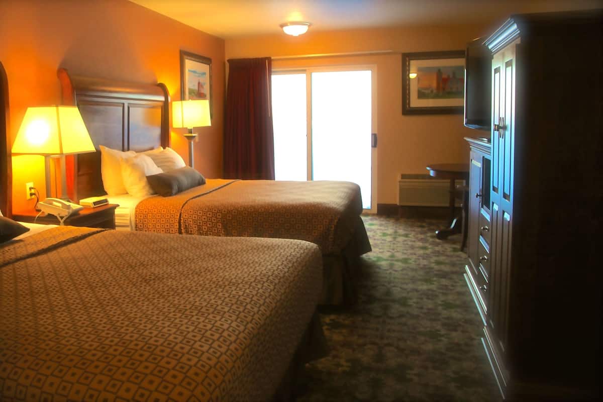 A hotel room with two beds, a desk with a lamp, a telephone, and a wardrobe.