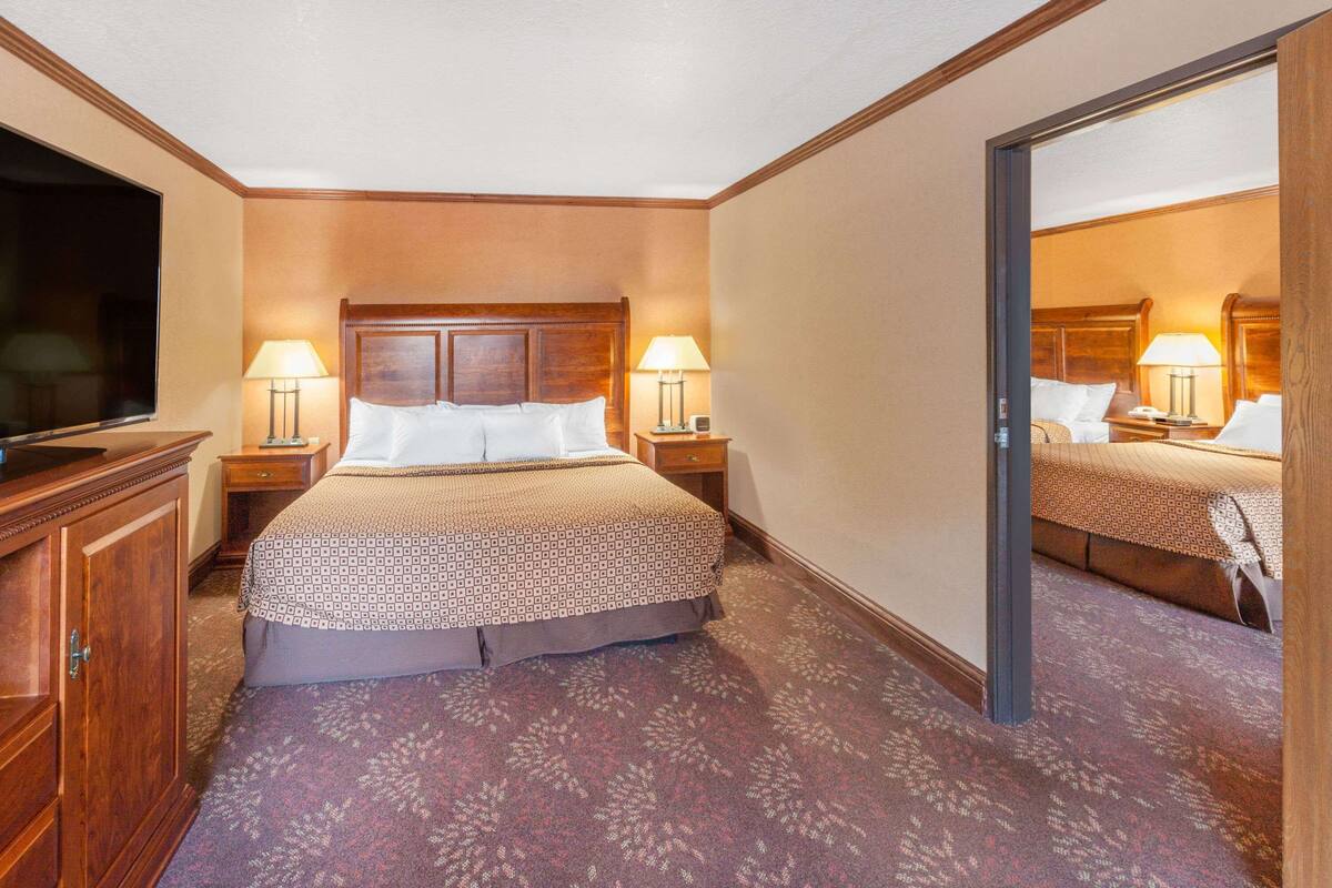 A hotel room with a large bed, two bedside tables with lamps, a wooden headboard, a wardrobe, and a television on the left side.