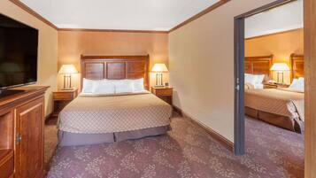 A hotel room with a large bed, two bedside tables with lamps, a wooden headboard, a wardrobe, and a television on the left side.