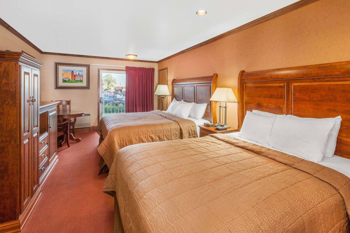 A hotel room with two beds, a desk, a chair, and a window with a view.