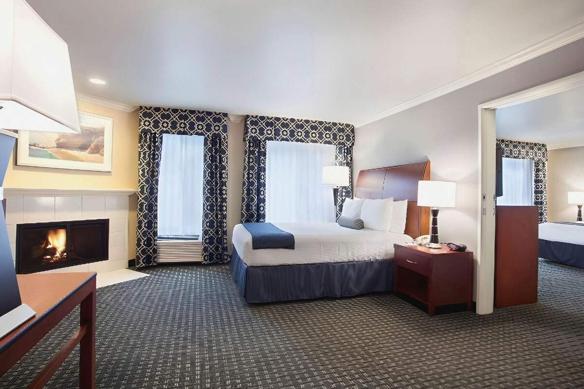 A hotel room with a bed, bedside tables, a fireplace, and patterned curtains.