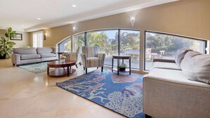 A spacious living room with a large window, a sofa, a coffee table, and a patterned rug. - Best Western Plus Marina Shores Hotel (Dana Point)