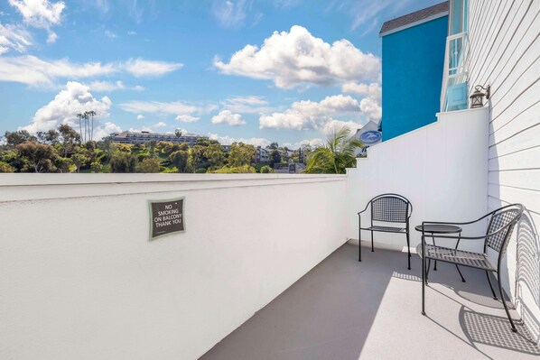 Un balcón con un letrero de ‘No Fumar’, dos sillas de metal y vistas a un edificio azul y árboles.