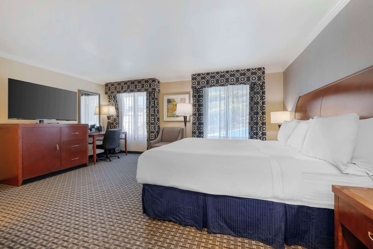 A hotel room with a large bed, a desk with a chair, a television, and a wardrobe.