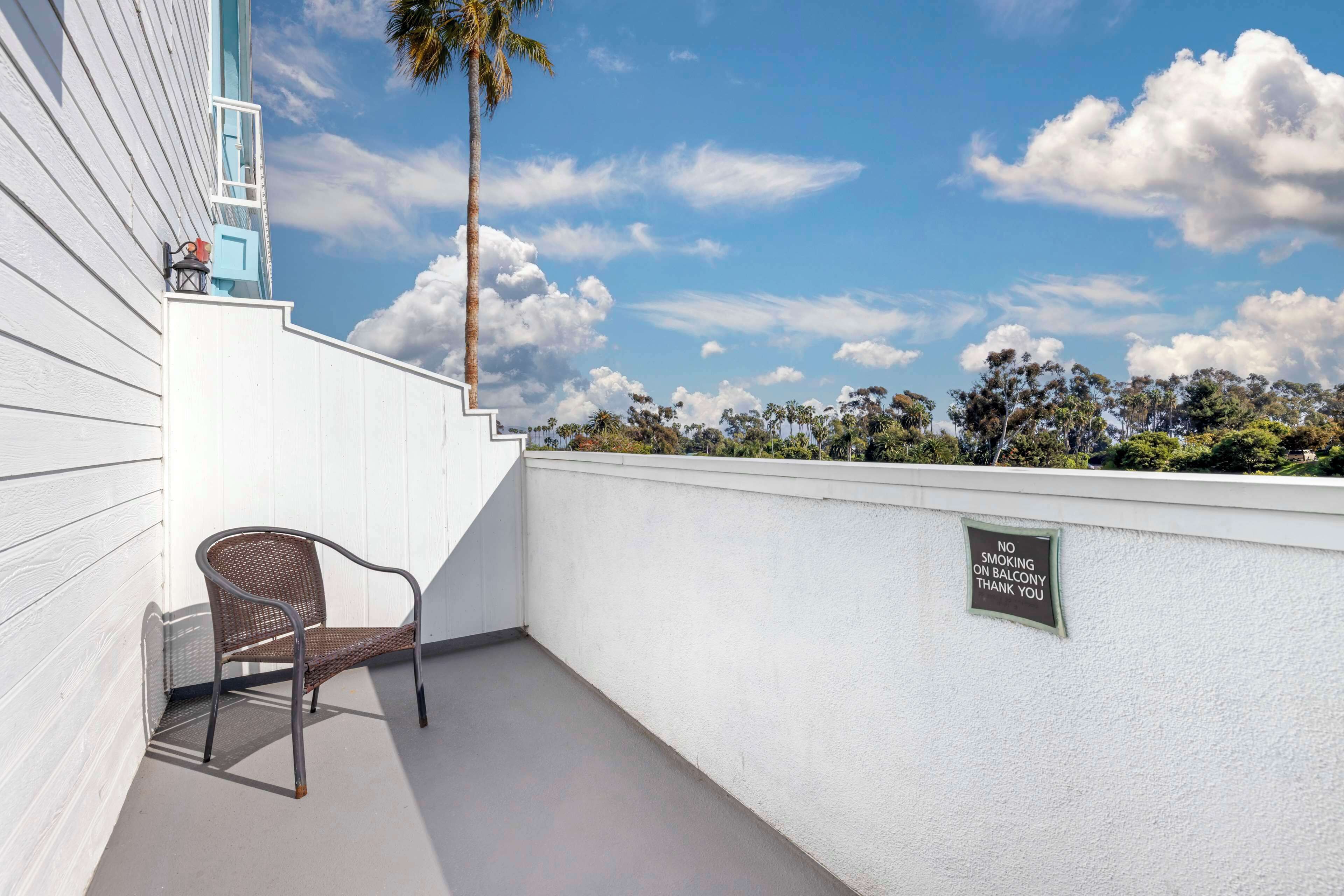 Ein Balkon mit einem Stuhl, einem Rauchverbot-Schild und Blick auf Bäume und Himmel.