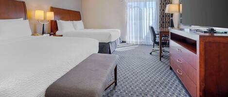A hotel room with two beds, a desk, a chair, a television, and a desk lamp.