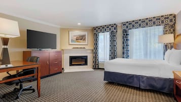 Una habitación de hotel con cama, escritorio, silla, televisión, chimenea y cortinas estampadas.