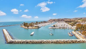 A marina with boats docked, a rocky breakwater, and a coastal town in the background. - Best Western Plus Marina Shores Hotel (Dana Point)