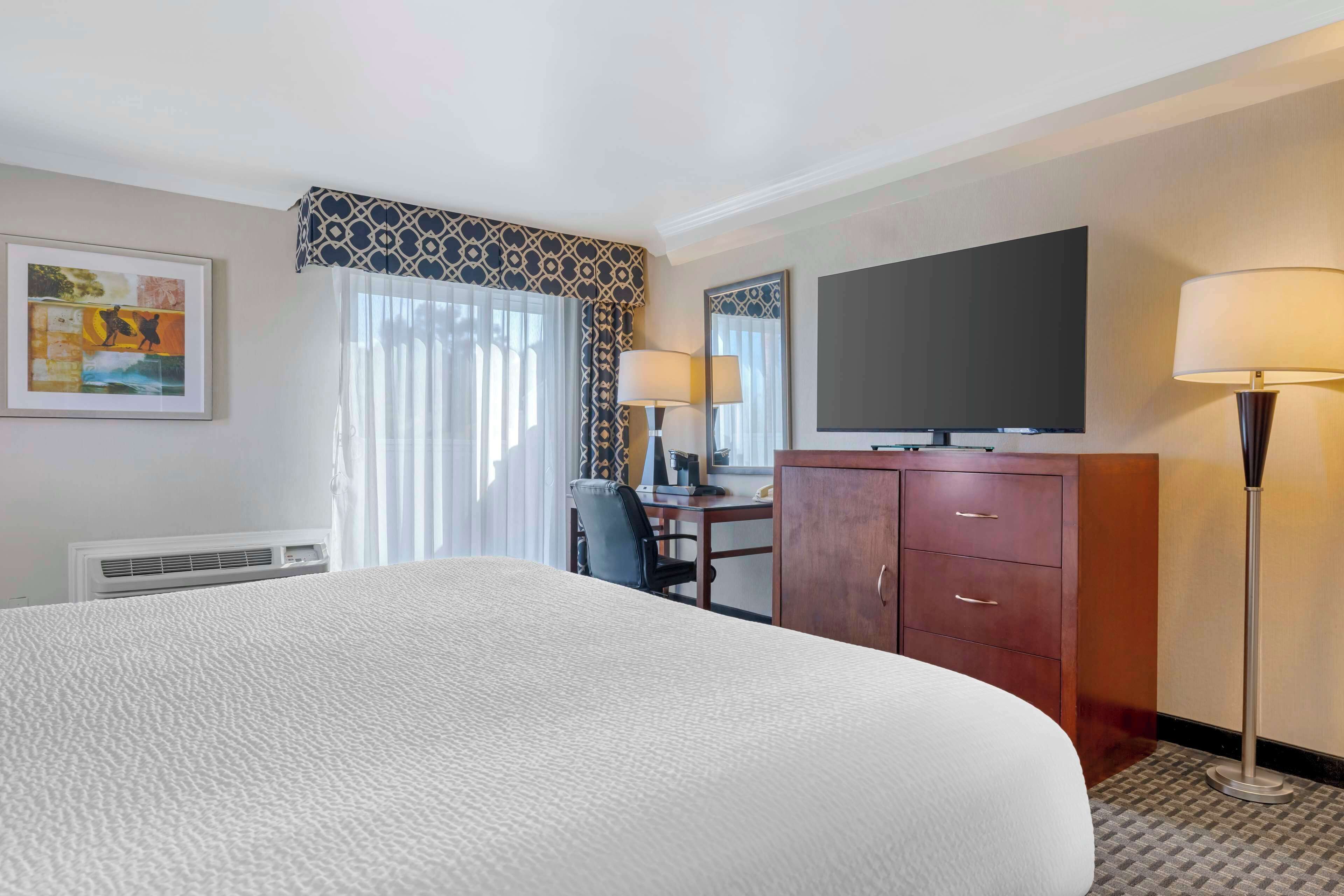 Una habitación de hotel con una cama grande, un escritorio con silla, televisor, armario y lámpara de pie.