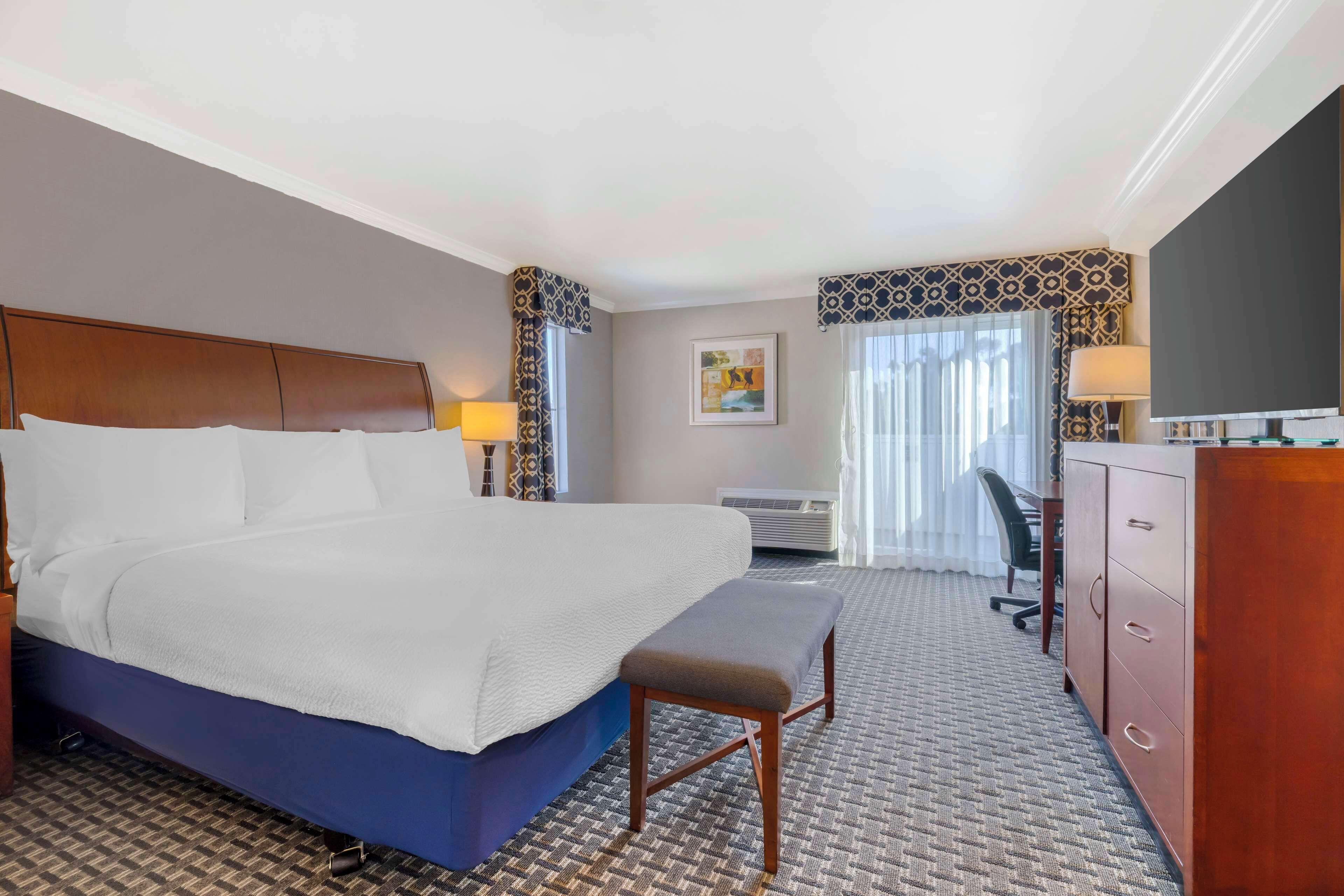 A hotel room with a large bed, a desk, a chair, a television, and a wardrobe.