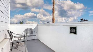 Un balcon avec deux chaises en métal, un mur blanc et un panneau indiquant «
Il est interdit de fumer
».