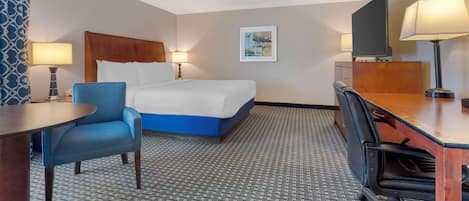 Una habitación de hotel con cama, escritorio, silla, televisor y lámpara.