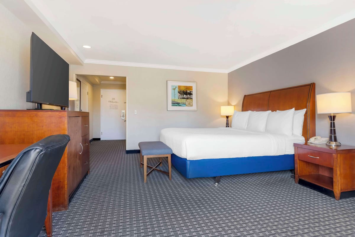 A hotel room with a bed, a desk, a chair, a TV, and a painting on the wall.