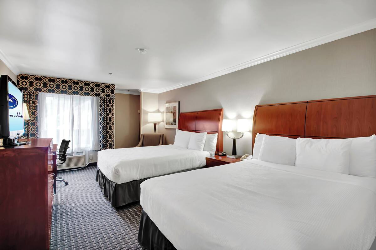 A hotel room with two beds, a desk, a TV, and a window with patterned curtains.