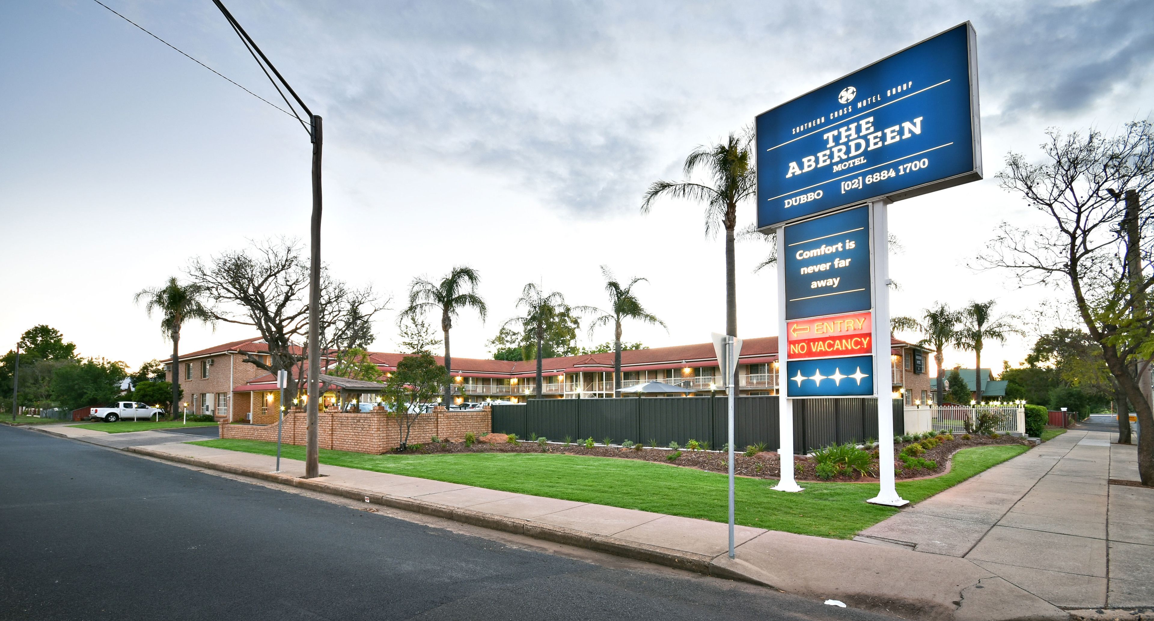 Un letrero de motel que indica 'no hay habitaciones disponibles', un edificio de ladrillo y un césped bien cuidado.