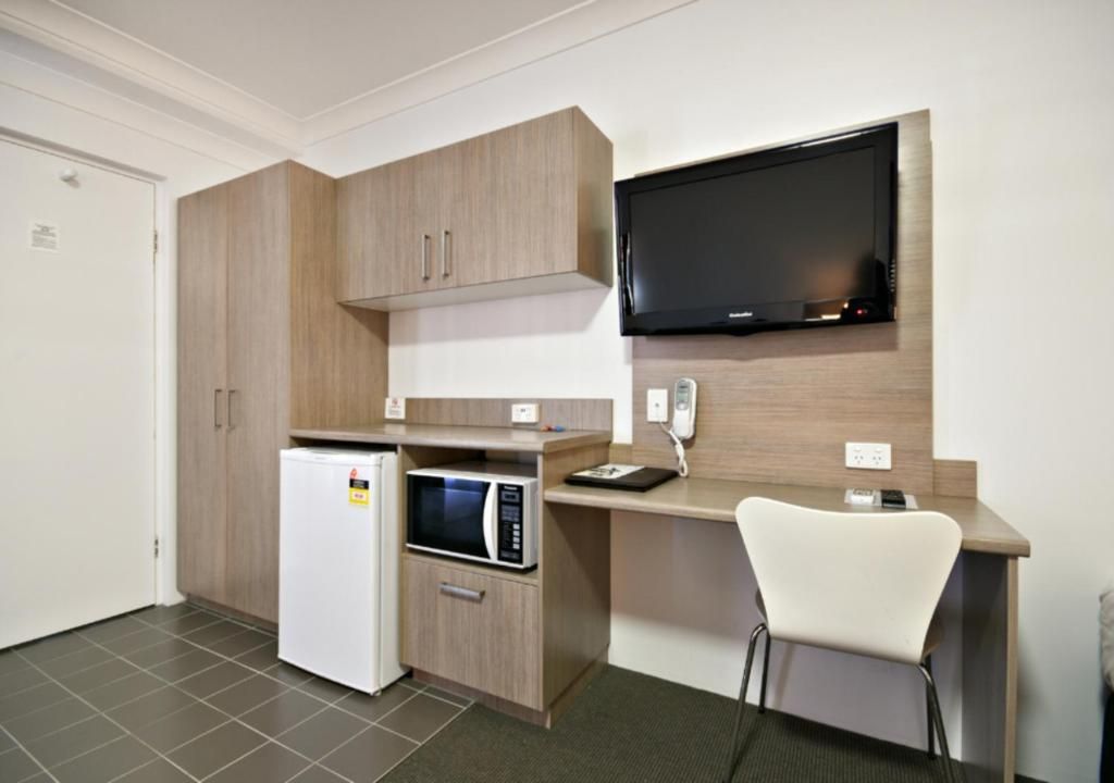 A compact kitchenette with a microwave, refrigerator, and a flat-screen TV mounted on the wall.