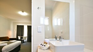 A hotel room with a bed, a desk, a chair, a large mirror, and a bathroom with a sink and toilet. - The Aberdeen Motel (Dubbo)