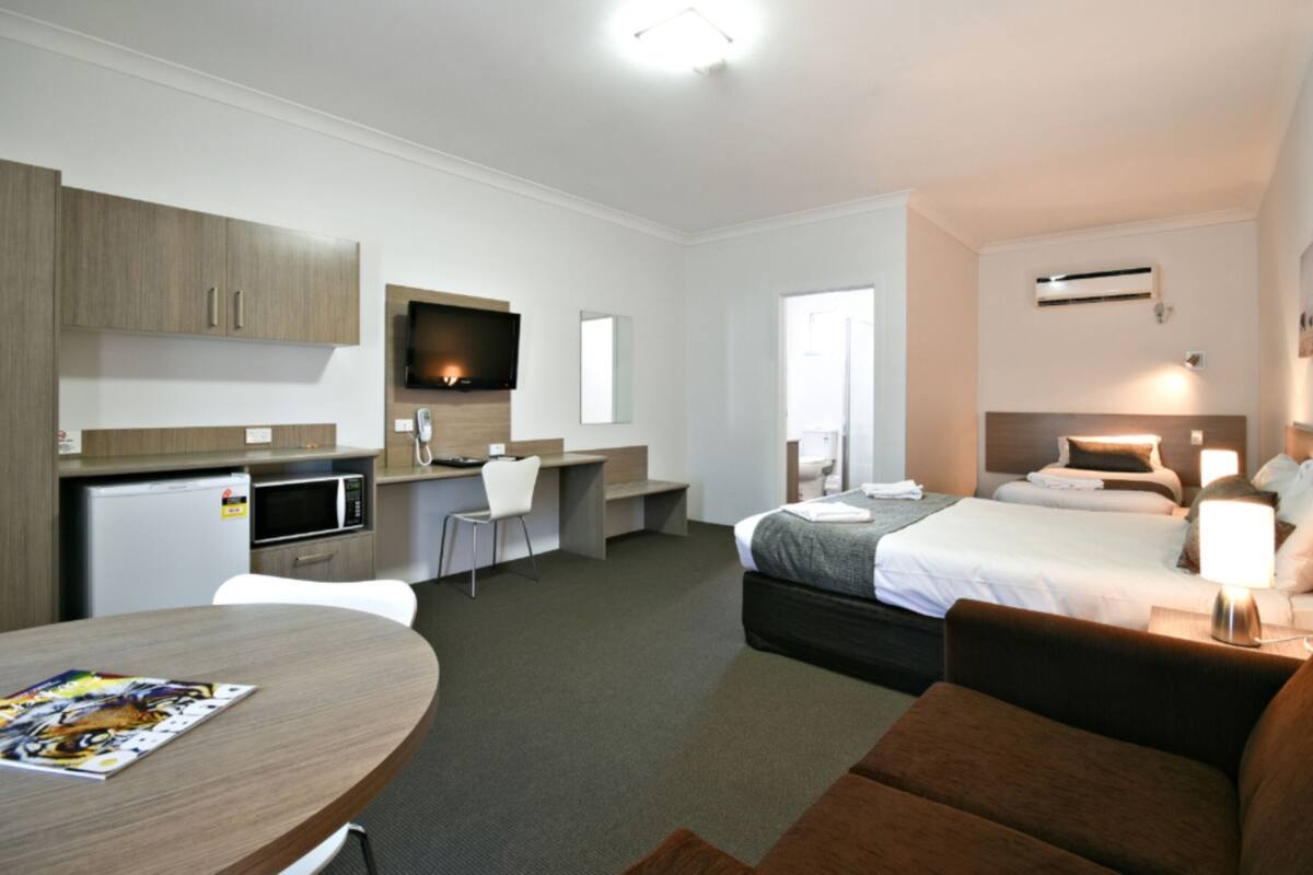 A hotel room with a kitchenette, a bed, a desk, and a TV.
