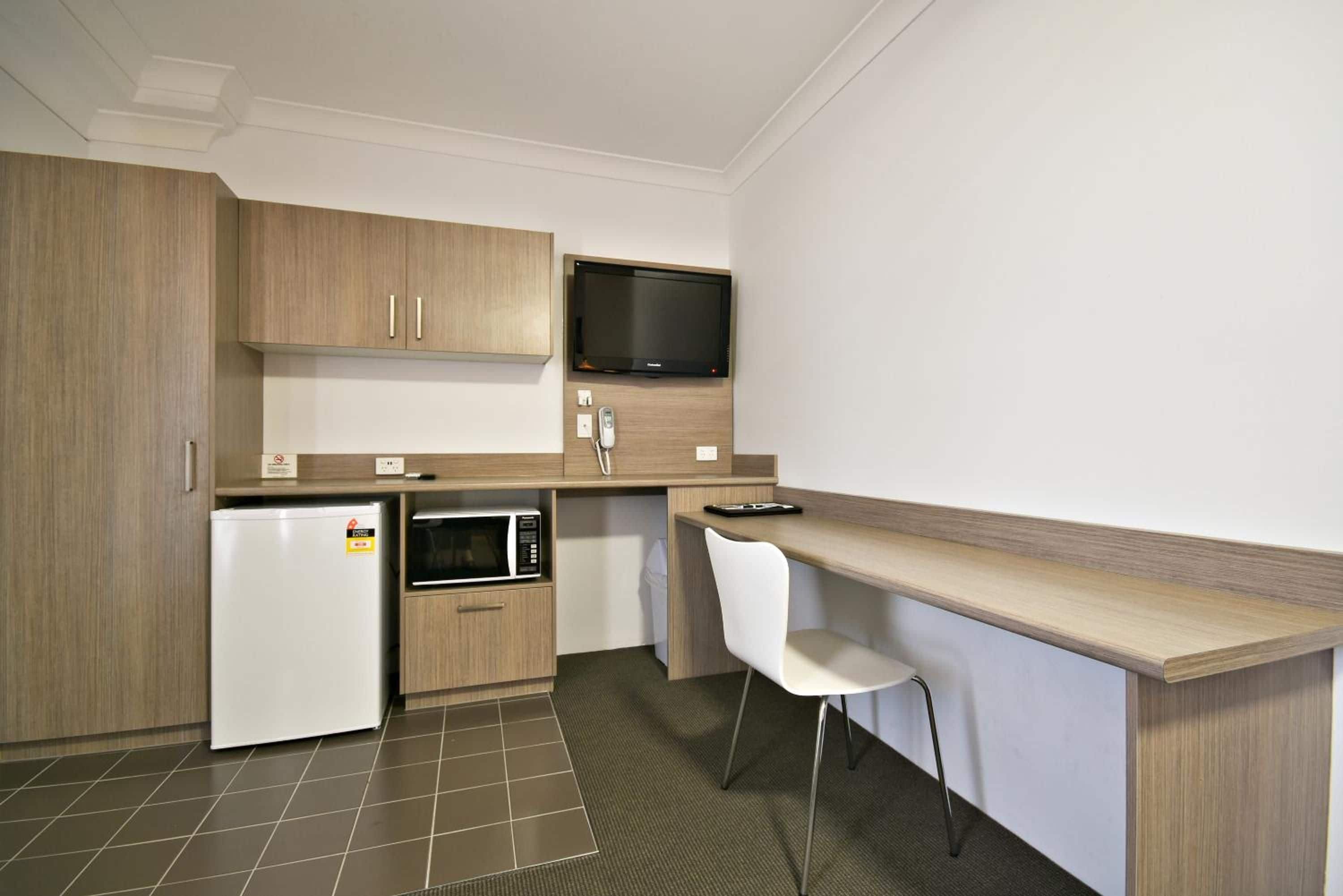 A compact kitchen with a refrigerator, microwave, and a flat-screen TV on the wall.