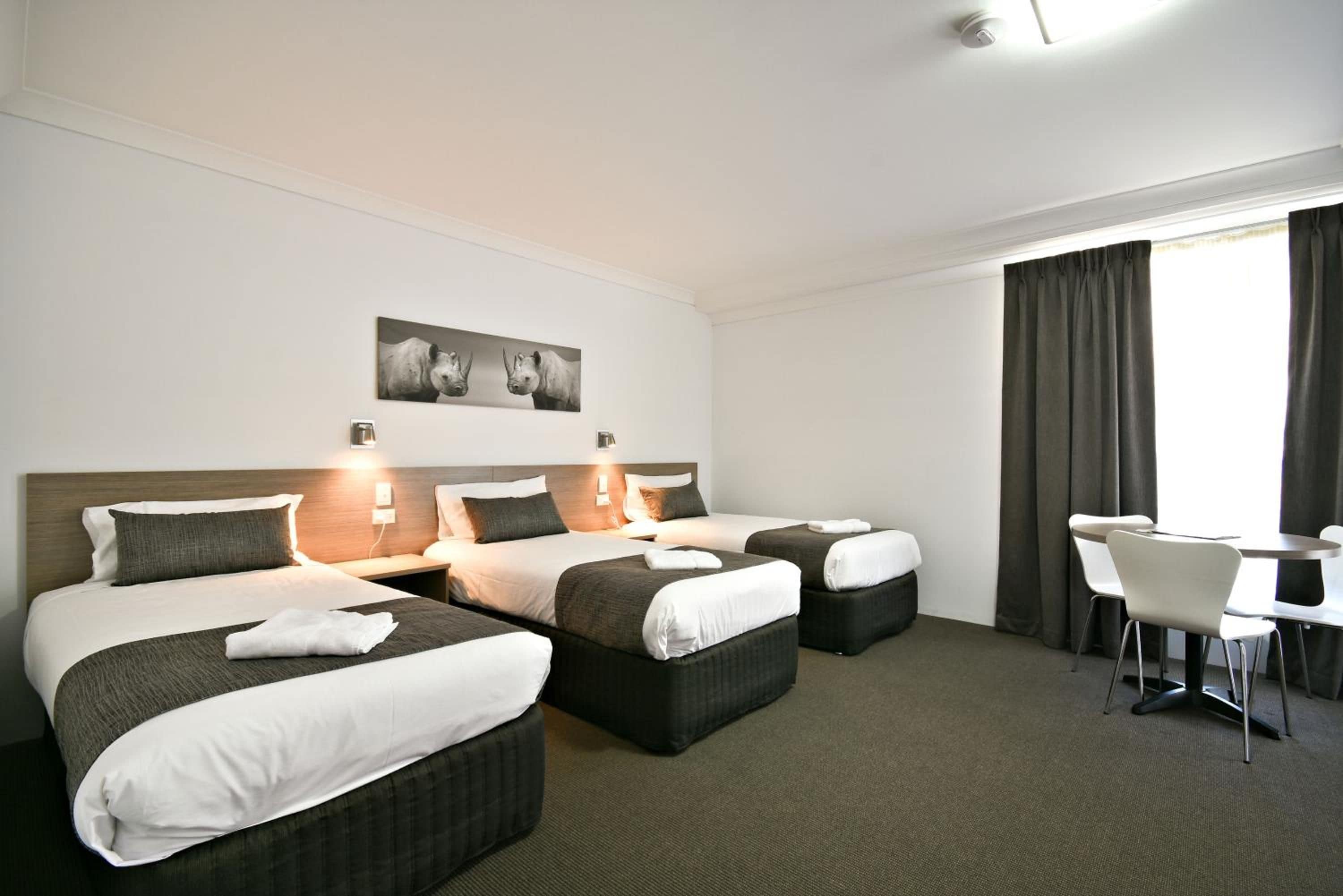 Een hotelkamer met twee bedden, een bureau en een stoel. Er is een raam met gordijnen.