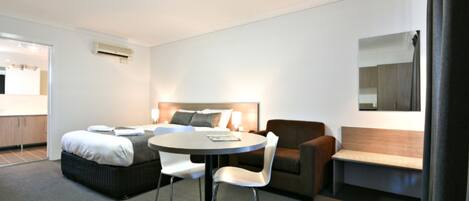 A hotel room with a bed, a round table with chairs, a sofa, a mirror, and a kitchenette area.