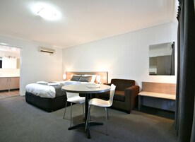 Una camera d'albergo con un letto, un tavolo rotondo con sedie, un divano, uno specchio e un angolo cottura.
