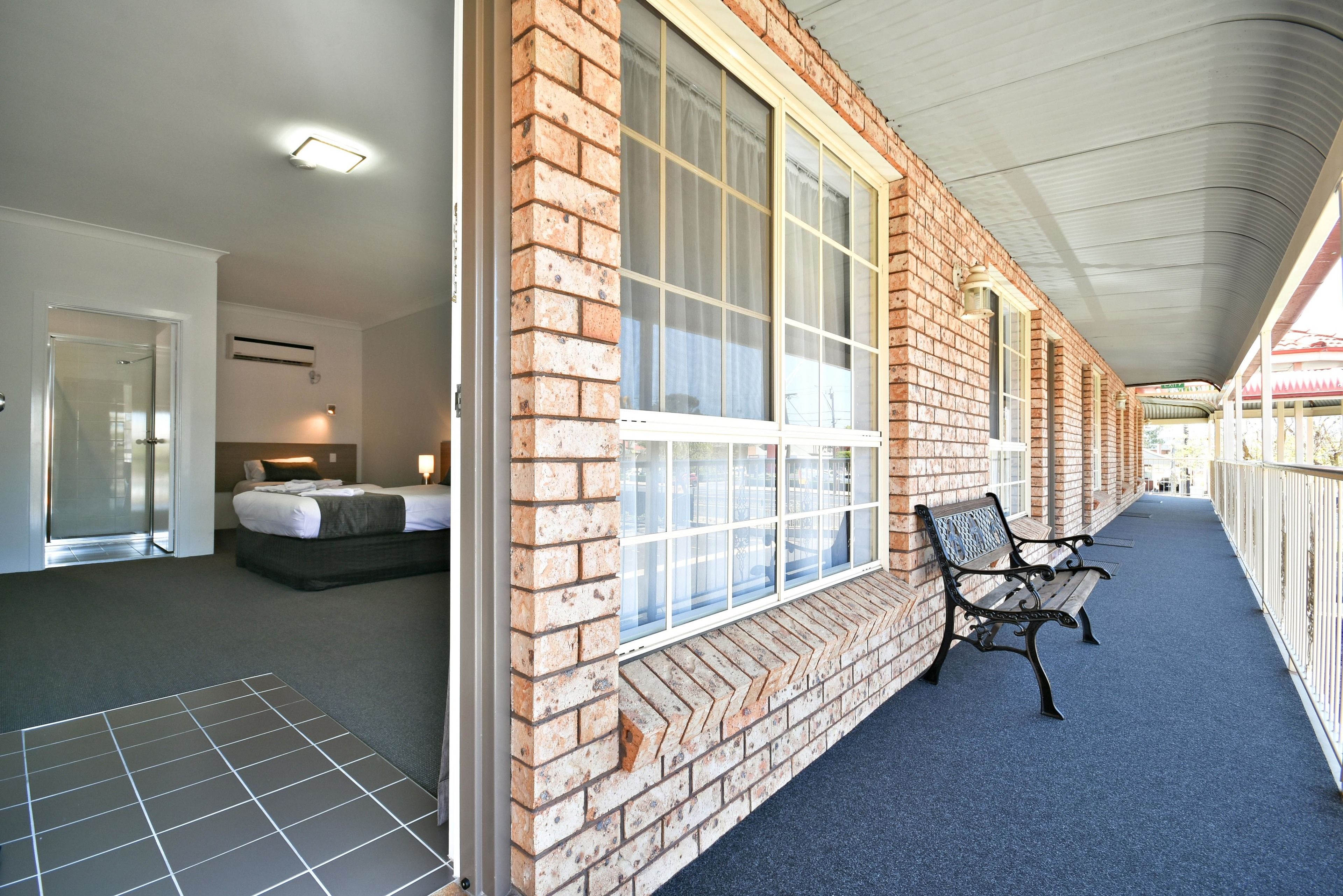 A hotel corridor with a brick exterior, large windows, a covered walkway, and a bench.