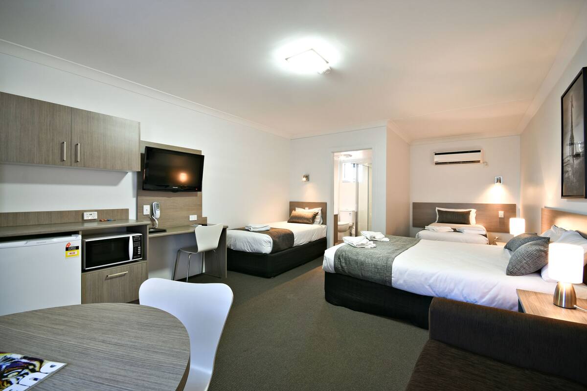 A hotel room with a kitchenette, two beds, a dining area, and a bathroom.