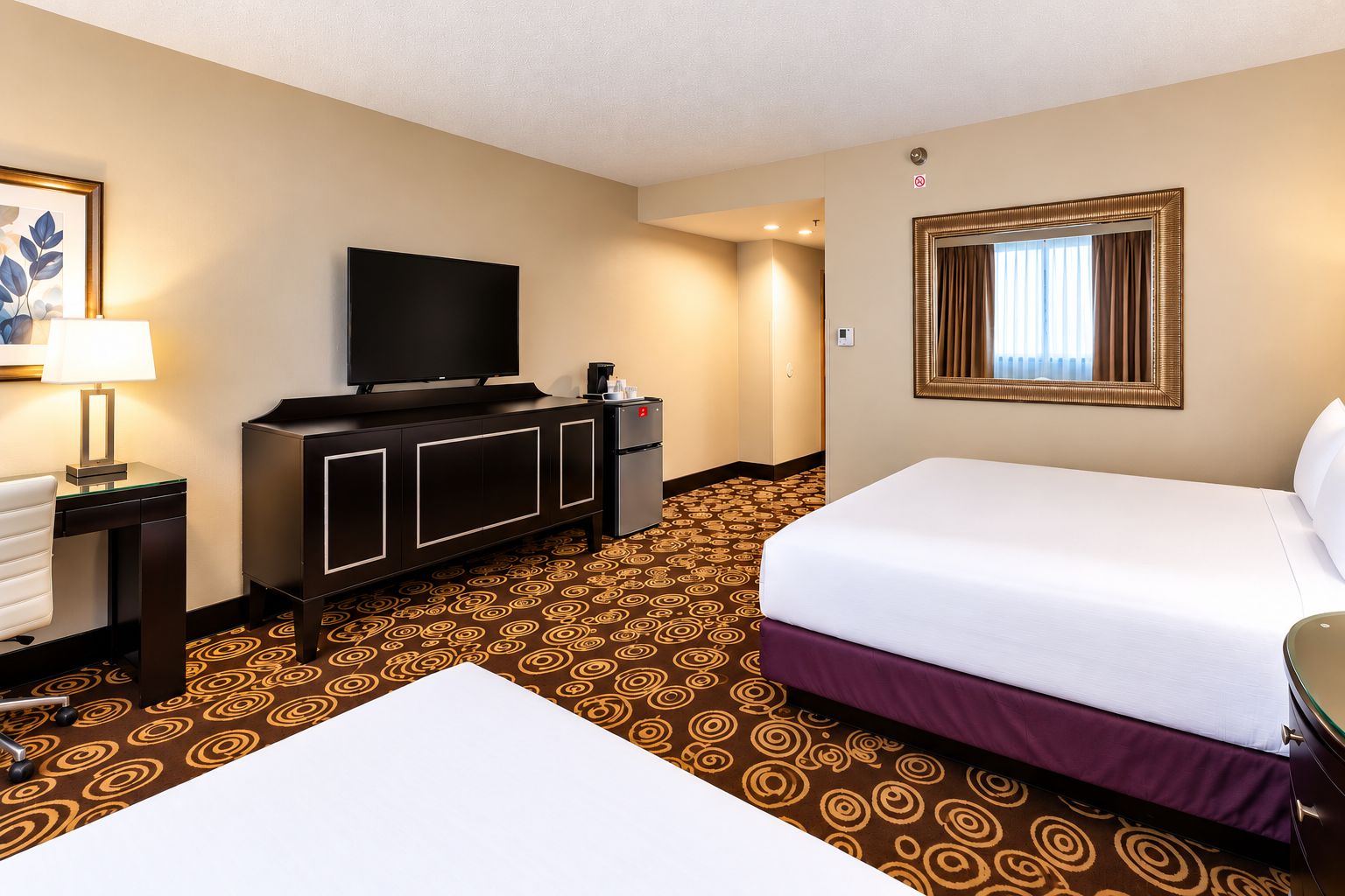 Una habitación de hotel con una cama, un escritorio con lámpara, una televisión y un minibar.