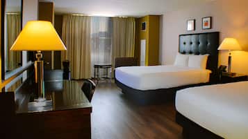 A hotel room with two beds, a desk, a chair, and a view of the city through large windows.